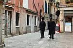 Orthodox jews from behind walking in Calle del Ghetto Vecchio street in front of a Kosher bar, in the Venetian Ghetto, Venice, Veneto, Italy Venice, Veneto, Italy - 07 28 2024: A view of the Venetian Ghetto with two orthodox jews walking in front of a Kosher bar, in summer.