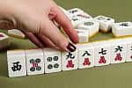 Mahjong, mahjongg, let's play it. A game of Chinese origin usually played by four persons with tiles resembling dominoes and bearing various designs, which are drawn and discarded until one player wins with a hand of four combinations of three tiles each and a pair of matching tiles.