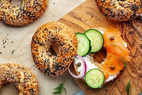 Assembling a lox bagel, overhead flat lay shot. Sandwich with smoked salmon Assembling a lox bagel, overhead flat lay shot. Sandwich with smoked salmon and fresh vegetables on a wooden cutting board and baking paper