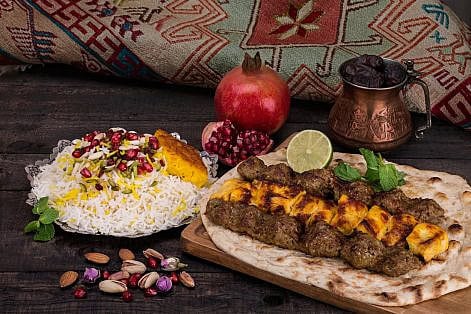 Traditional Middle eastern Persian chicken and lamb meat Shashlik Kebab (skewered meat) BBQ Grill on flat pita bread and saffron rice and tahchin and pomegranate on a dark background. Iranian cuisine Traditional Middle eastern Persian chicken and lamb meat Shashlik Kebab (skewered meat) BBQ Grill on flat pita bread and saffron rice and tahchin and pomegranate on a dark background. Iranian cuisine