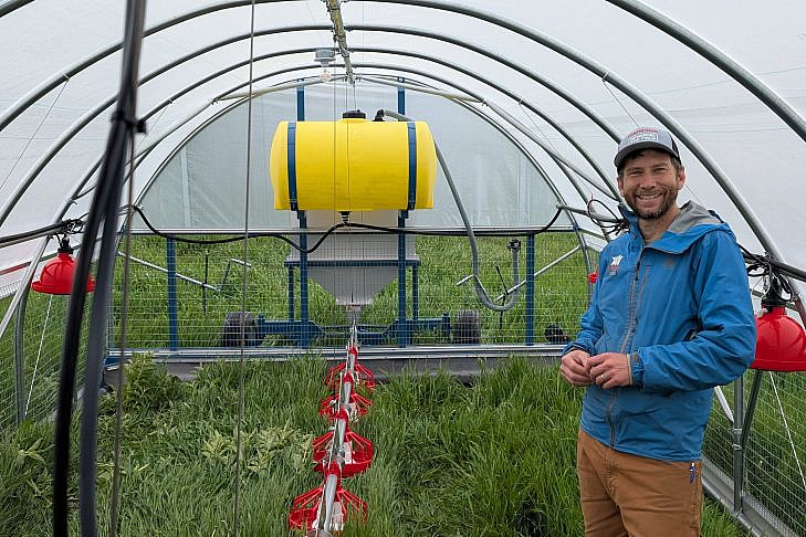 Zalman Friedman Inside a Mobile Coop Zalman Friedman standing inside a hoop-style mobile coop next to a feed tank and a line of red poultry waterers, with green pasture visible outside.